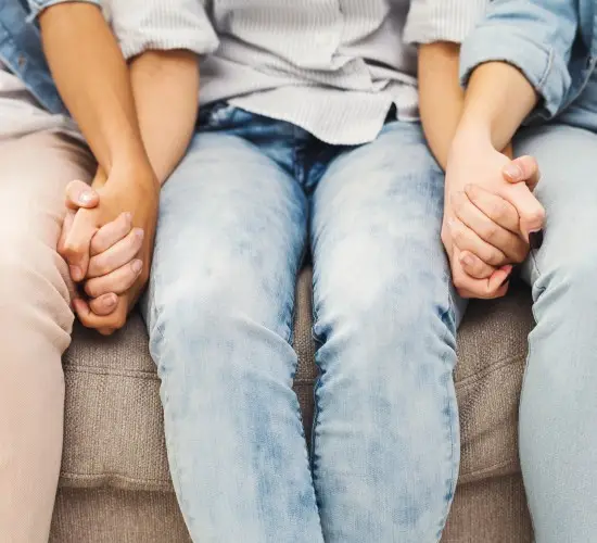 Three people sitting next to each other holding hands