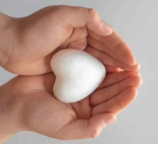cupped hands holding a white heart-shaped object